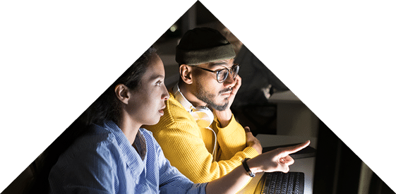 Side view portrait of several people working in dark office at night, focus on two colleagues using computer in foreground, copy space